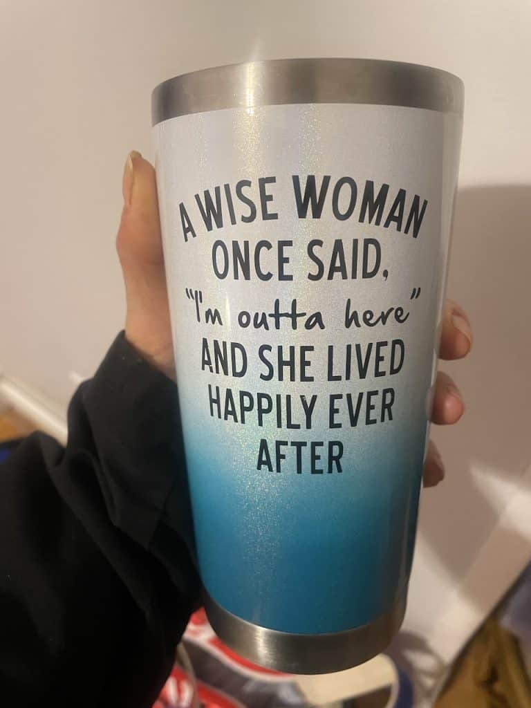 A hand holds a blue and cream, insulated mug with a catchy phrase, photo ©Kate Dana