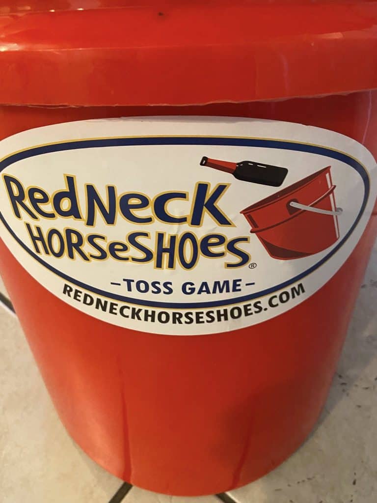 A red plastic bucket with a sticker announcing Redneck Horseshoes, a bottle toss game from Charleston, S.C.