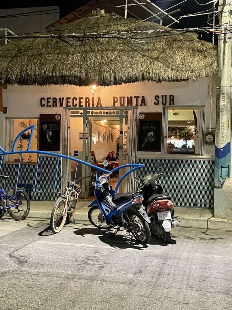 A nighttime scene of cervezeria punta sur with a thatched roof and motorcycles out front on Isla Cozumel, Mexico, photo ©Kate Dana