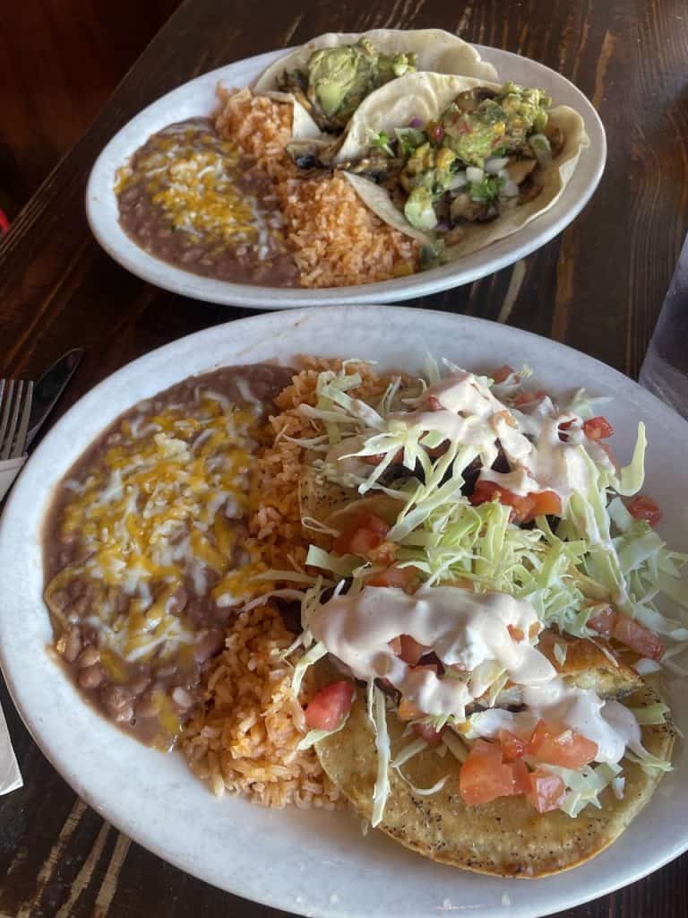 Two plates piled high with tacos, beans, rice, and vegetables, photo ©Kate Dana