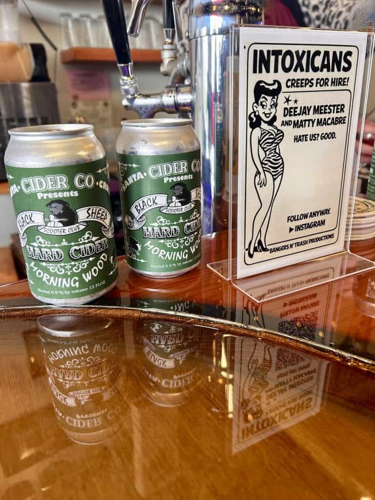 Green and black aluminum cider cans created for the Black Sheep Scooter Club Morning Wood Vintage Rally sit on a bar at the Santa Cruz Cider Co. in Watsonville, CA, photo ©Kate Dana