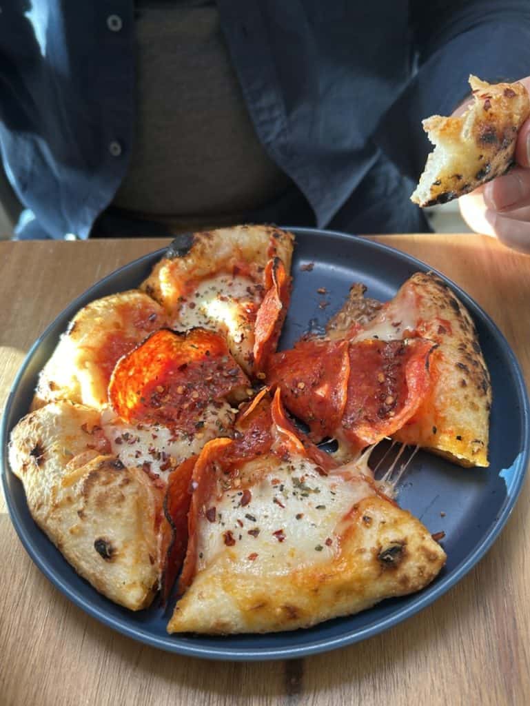 A small pizza with pepperoni on a plate on a table, photo ©Kate Dana