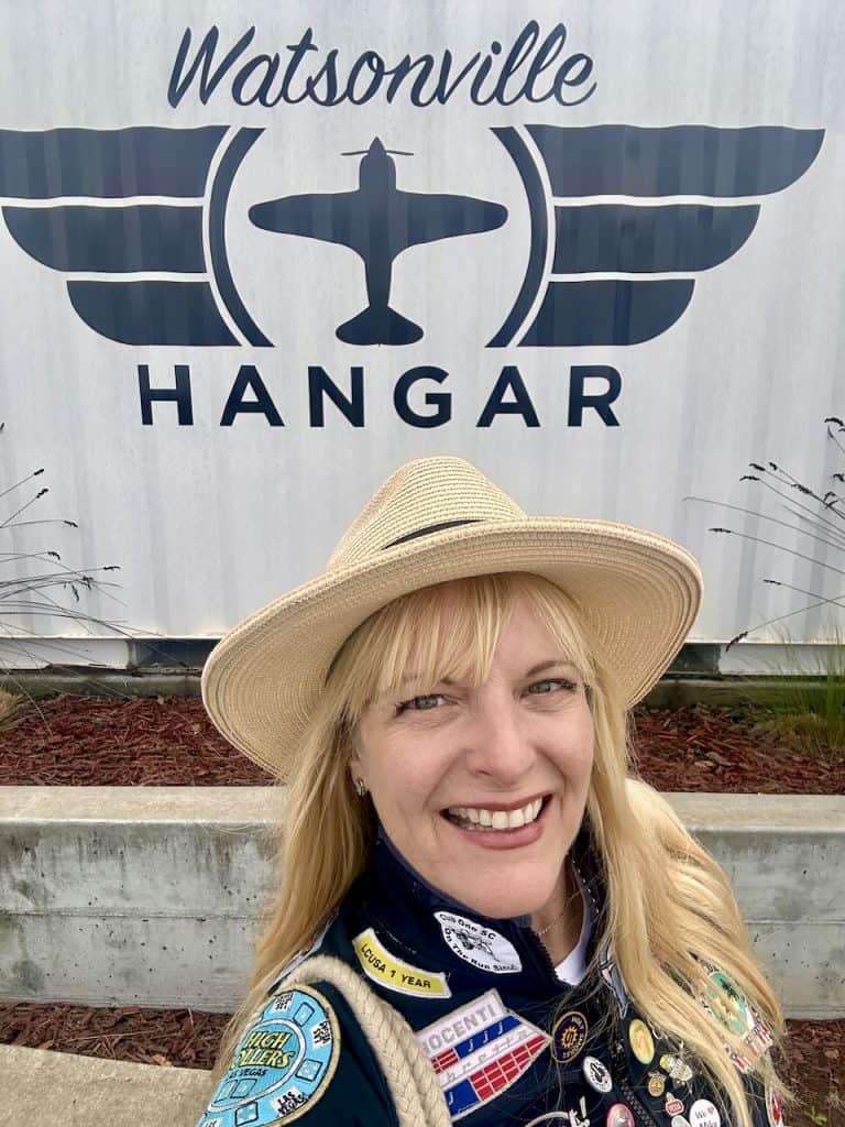 Cocameca founder Kate Dana smiles in front of a sign with an aviation theme for The Hangar in Watsonville, CA, photo ©Kate Dana