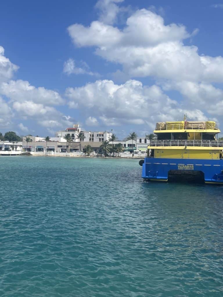 a view of Isla Cozumel, Mexico with a yellow ferry boat docked over a bright blue ocean, photo ©Kate Dana