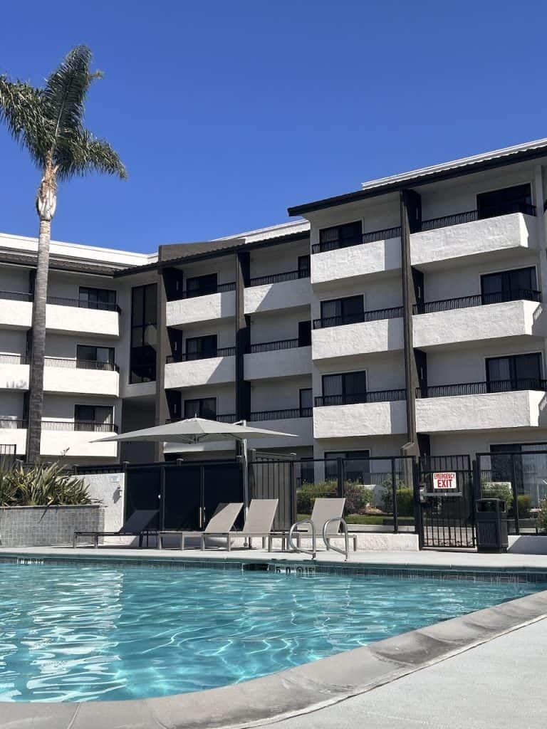 The exterior of a hotel with a blue swimming pool and palm trees ©Kate Dana