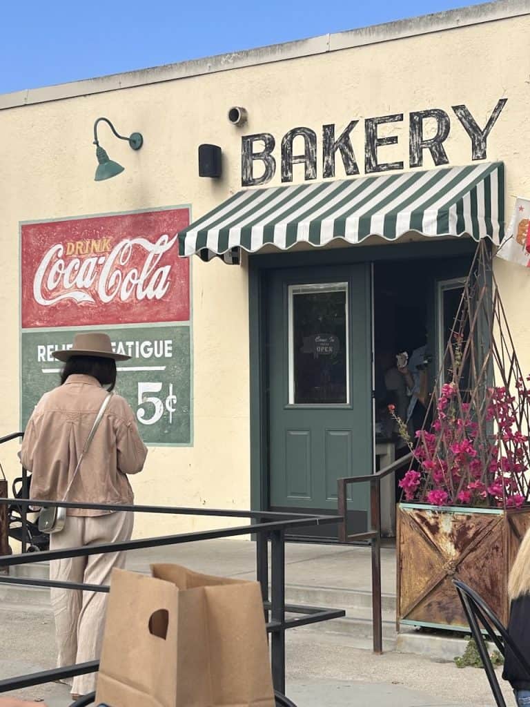A person stands outside of a trendy bakery near hand painted signs, photo © Kate Dana