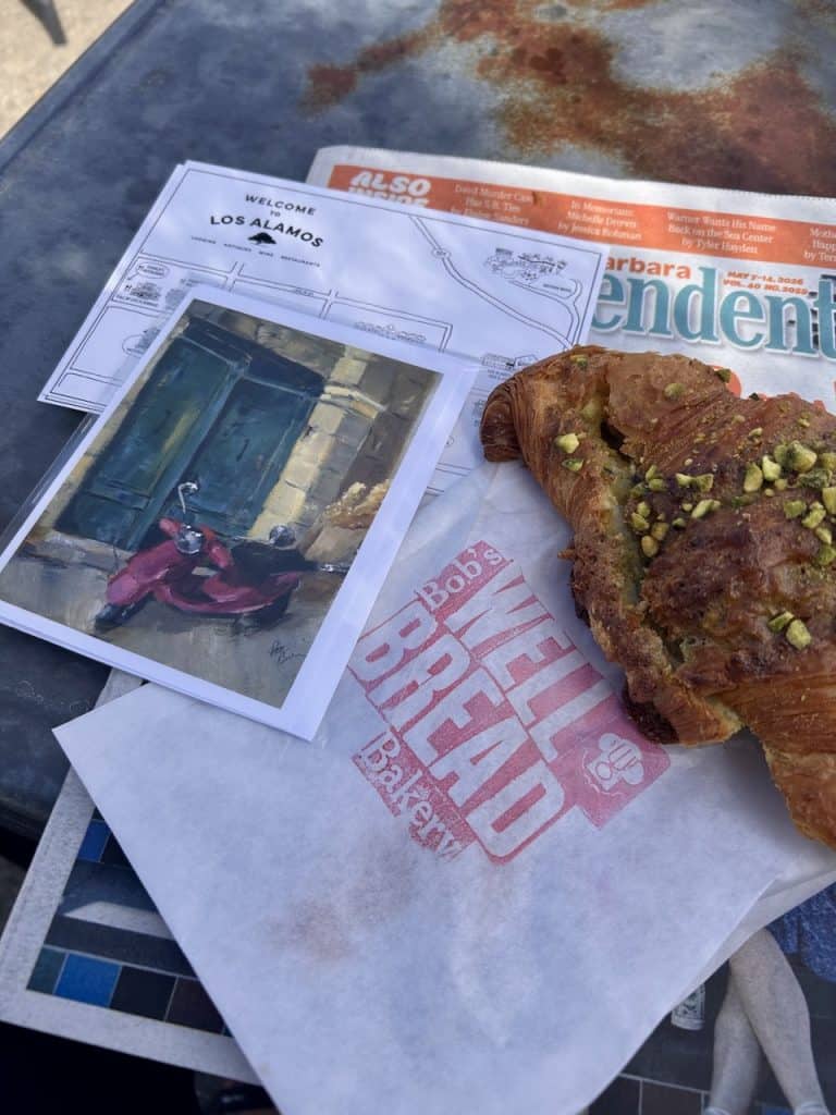 A rustic tabletop with a postcard and a buttery, pistachio croissant. photo © Kate Dana