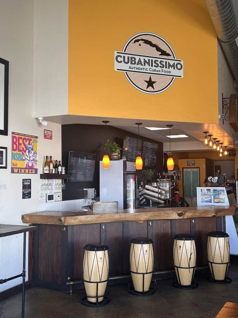 A sunny yellow wall inside the eatery Cubanissimo with bongo drum-shaped stools at a bar, photo ©Kate Dana