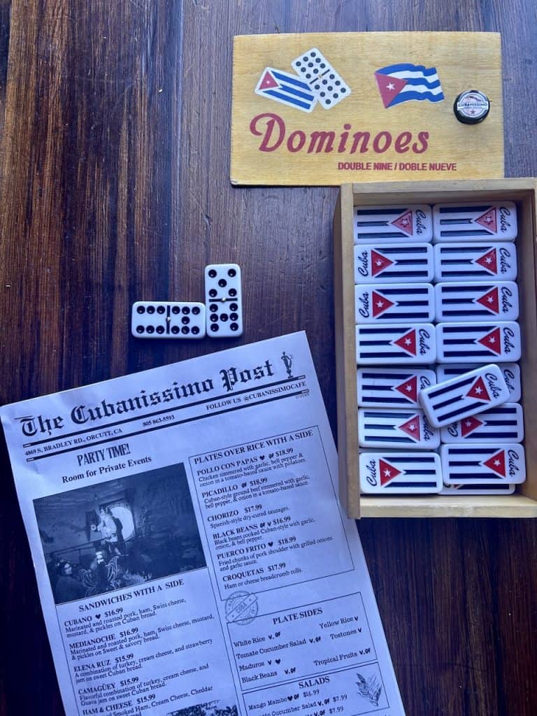 A table shows colorful Cuban flag dominoes and a newsletter announcing The Cubanissimo Post, photo ©Kate Dana