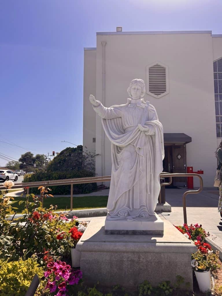 A white statue of St. Louis de Montfort outside of a church on a sunny day, photo © Kate Dana