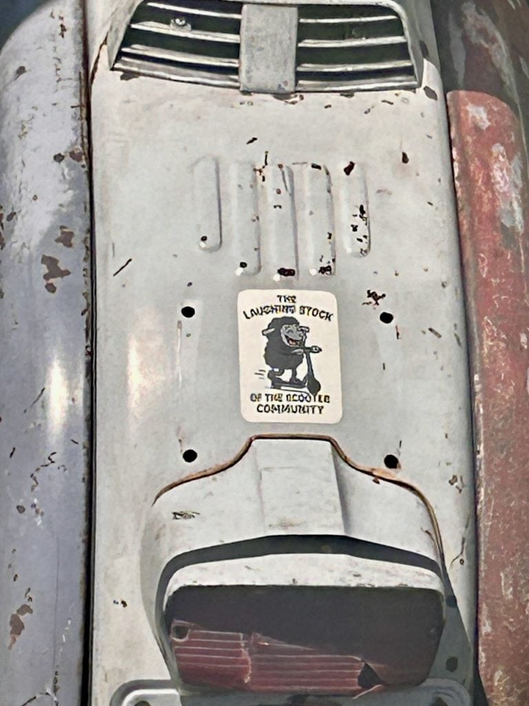 A sticker on the back fender of a scooter reads, "The Laughing Stock of the Scooter Community" photo ©Kate Dana