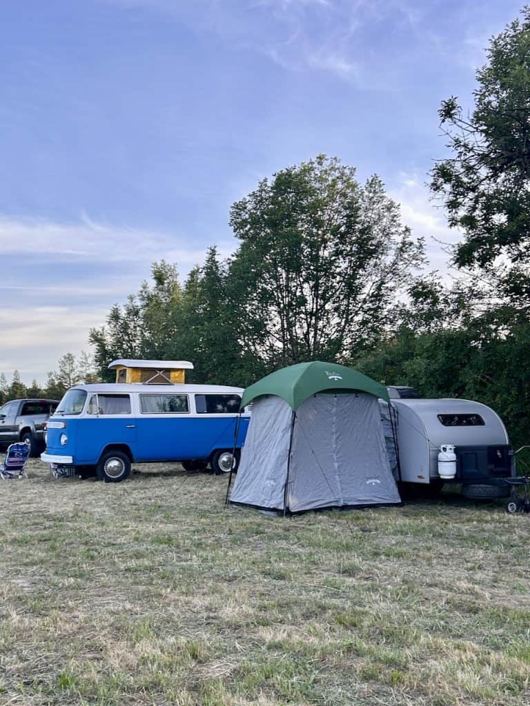 A VW Camper bus, a tent, and a small trailer on a field campground, photo ©Kate Dana