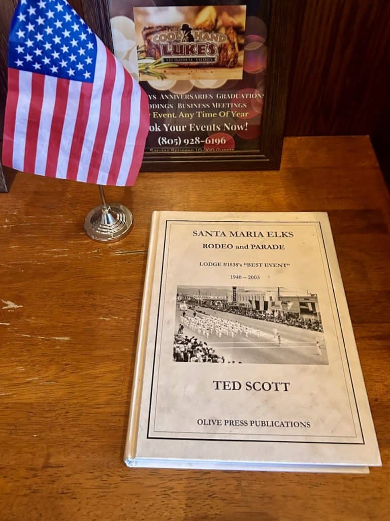 A book about the Santa Maria Elks Rodeo and Parade rests on a wooden table next to a small American flag, photo ©Kate Dana